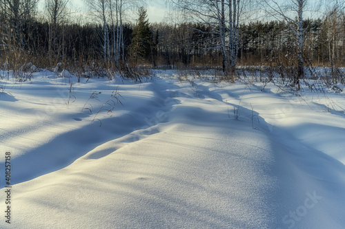 Snow-covered road with ruts close-up. Grains of snow are visible near, and birches in the distance. Winter sunny day