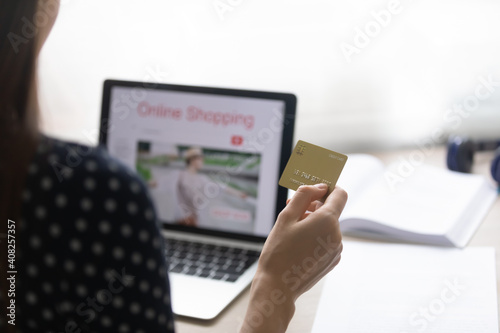Close up of young woman shopper sitting by pc screen holding credit card preparing to make purchase online. Millennial female choose easy convenient secure electronic payment planning to get cashback