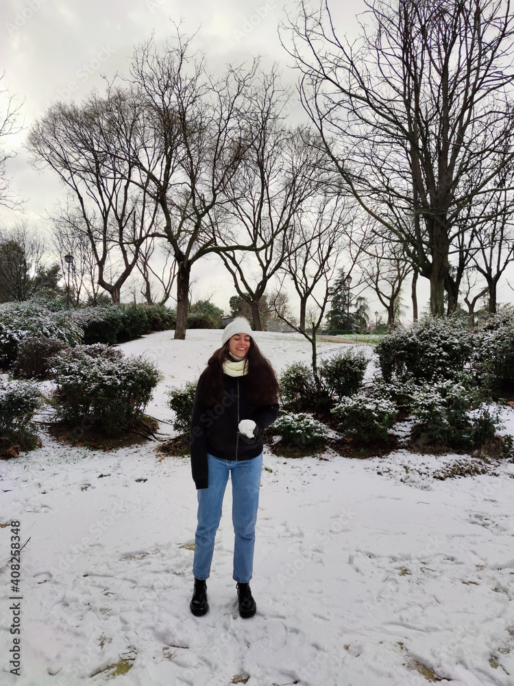 Woman smiling in a snowy park with a snowball in her hand.