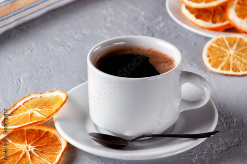 Cup of coffee with dried oranges on gray background