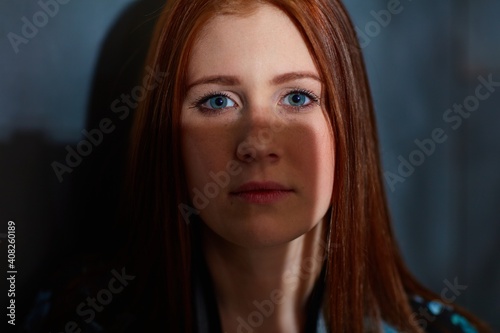 Closeup portrait of ginger woman with blue eyes partly in shadow.