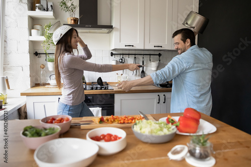 Foto Defend yourself, my lady Laughing young spouses cook vegan food on weekend in good playful mood