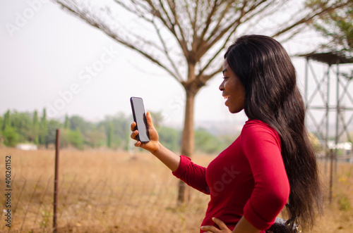 young black beautiful lady standing and using her smart phone in the park