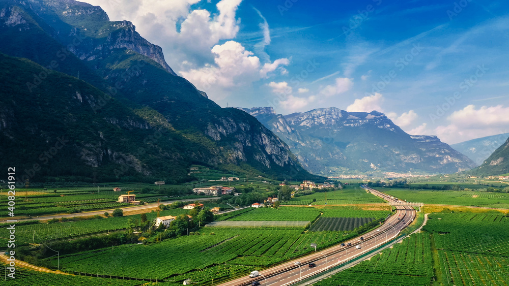 Fototapeta premium Aerial Drone View: Beautiful Farmlands of Italy Located in the Mountains. Highway Lying in the Mountainous Region. Vineyards, Olive Trees, Various Vegetable Growing Fields and Agricultural Plantations