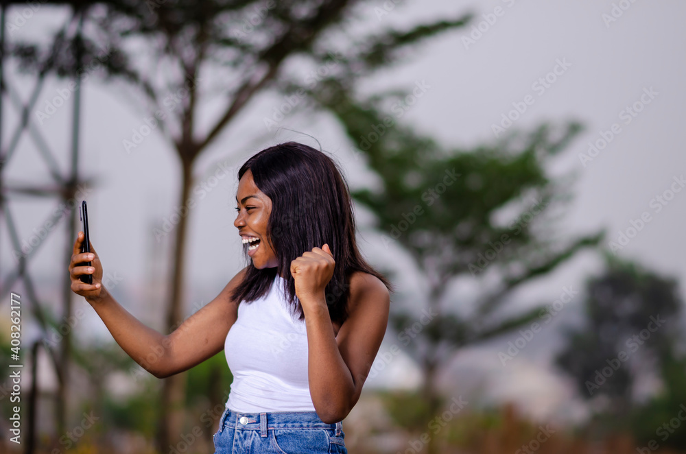 young black beautiful lady standing and using her smart phone in the park