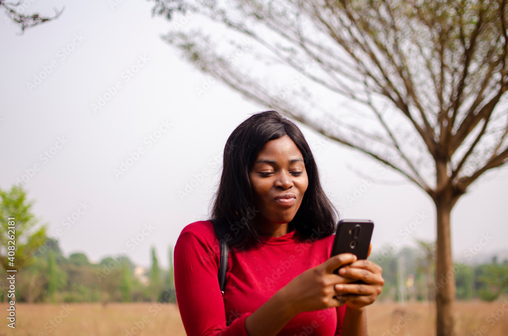 young black beautiful lady standing and using her smart phone in the park young black beautiful lady standing and using her smart phone in the park