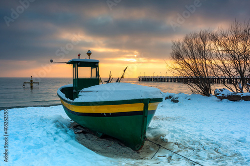 Fototapeta Naklejka Na Ścianę i Meble -  Fishing boat on snowy beach in Gdynia Orlowo at sunrise, Baltic Sea. Poland
