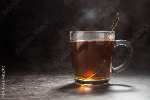 Tea in a transparent mug with a spoon steamed on a gray background