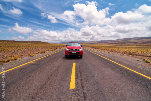 Red car driving on asphalt road on cloudy day in Atacama desert, Chile