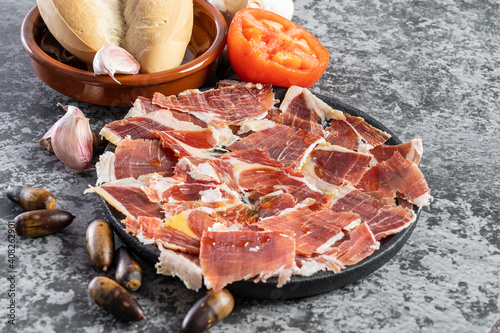 Close up of jabugo serrano ham slices with acorns, tomatoes, garlic and olive oil, Dry Spanish ham. Typical spanish breakfast concept. Black background 