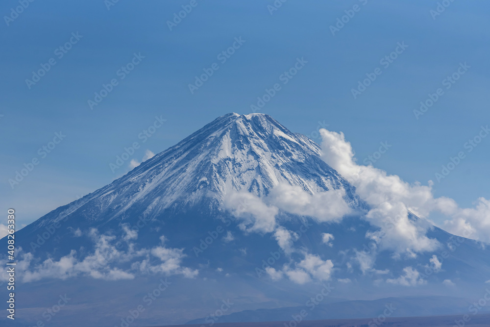 Majestic view of snowy volcanic mountain Licancabur surrounded by clouds on sunny day under blue sky