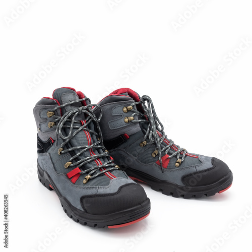 Trekking boots for men made of natural nubuck and synthetic mesh. Gray with red and black trim. Metal fittings. Grooved outsole. Isolated over white background.