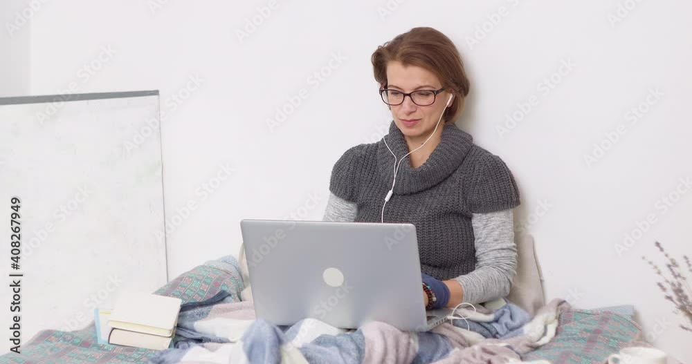 Young woman staying at home uses laptop to study online. Female working on the computer with headphones while sitting in the room. Young woman staying at home uses laptop to study online. Female working on the computer with headphones while sitting in the room.