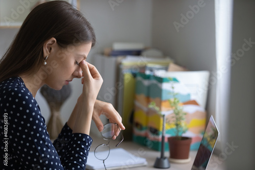 Problems with eyes. Tired young female student taking glasses off rubbing nose bridge feeling overworked by laptop computer screen. Stressed lady freelancer suffering of pain headache dry eye syndrome