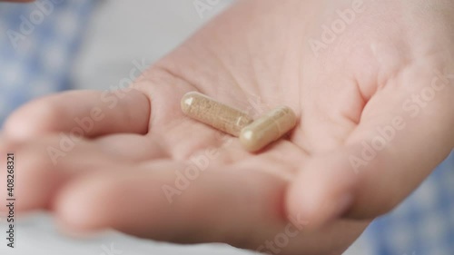 Two big transparent cylindrical pill capsules with green powder inside fall into palm of hand from pill bottle. Close-up, front view, center composition