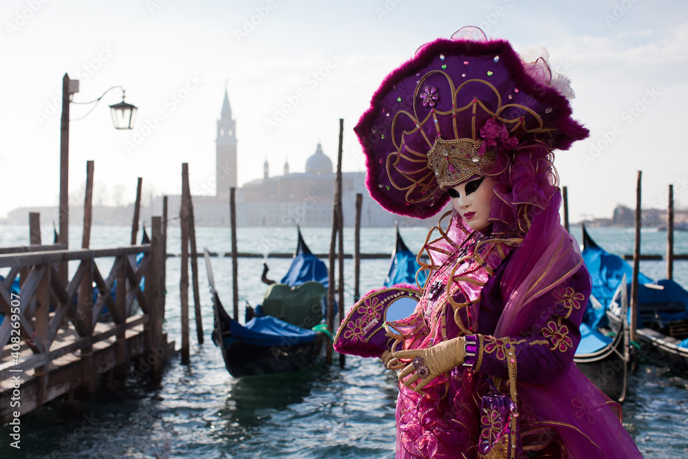 Masked woman in ornate costume at the the Venetian masquerade stands against stone wall near the Grand canal in Venice