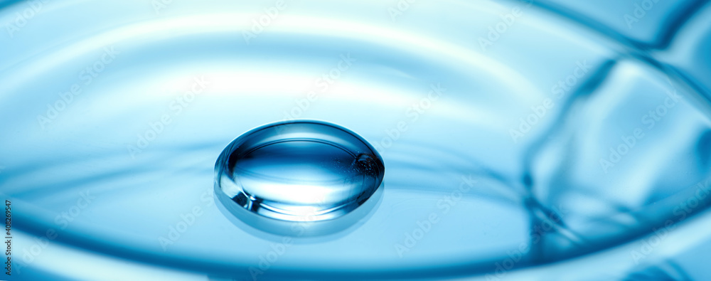 Clean glass petri dish with liquid drop inside over blue light background