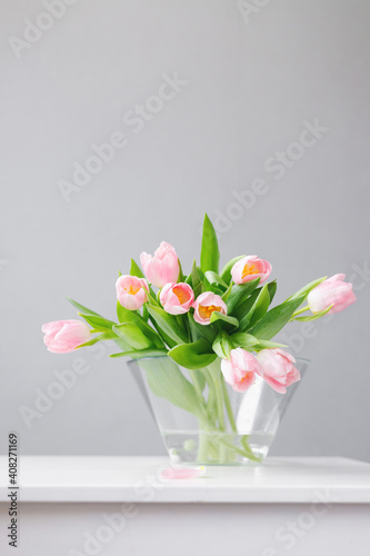 Fototapeta Naklejka Na Ścianę i Meble -  pink tulips in a large glass vase stand on the table, on a gray background, space for text, free space, floristry, florist, tulip bouquets, bouquet, valentine's day, international women's day,flowers