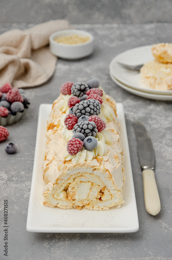 Meringue roll Pavlova cake with cream and raspberries, blackberries and blueberries on top on a gray background. Copy space. Meringue roll Pavlova cake with cream and raspberries, blackberries and blueberries on top on a gray background. Copy space.