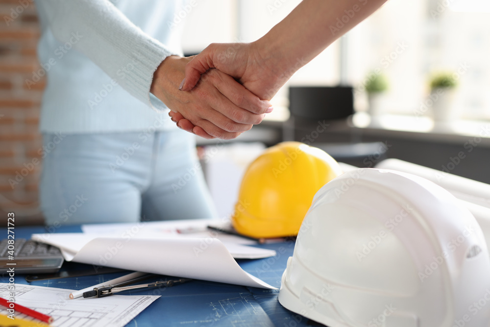 Over construction sketches, designer and client shake hands with each other Over construction sketches, designer and client shake hands with each other