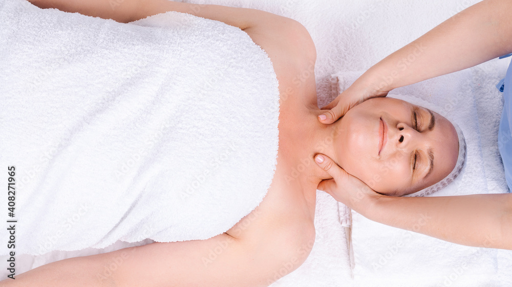Senior Caucasian woman wrapped in white towel and hands of a master doing neck massage. Photo from above. Senior Caucasian woman wrapped in white towel and hands of a master doing neck massage. Photo from above.