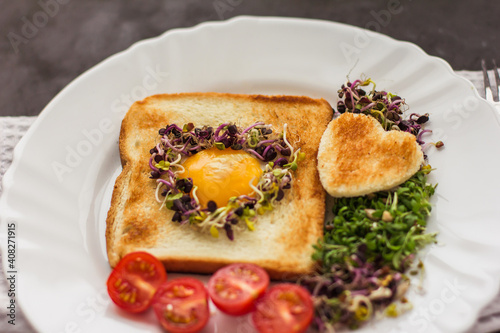 Egg in a hole of bread heart shape, microgreens, healthy food Breakfast, tea, black background