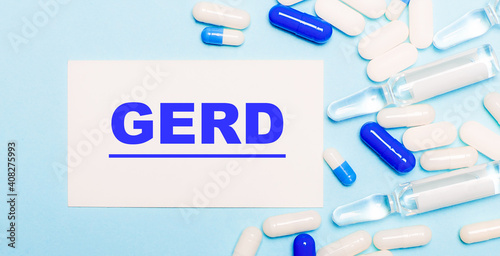 Pills, ampoules and a white card with the text GERD on a light blue background. Medical concept
