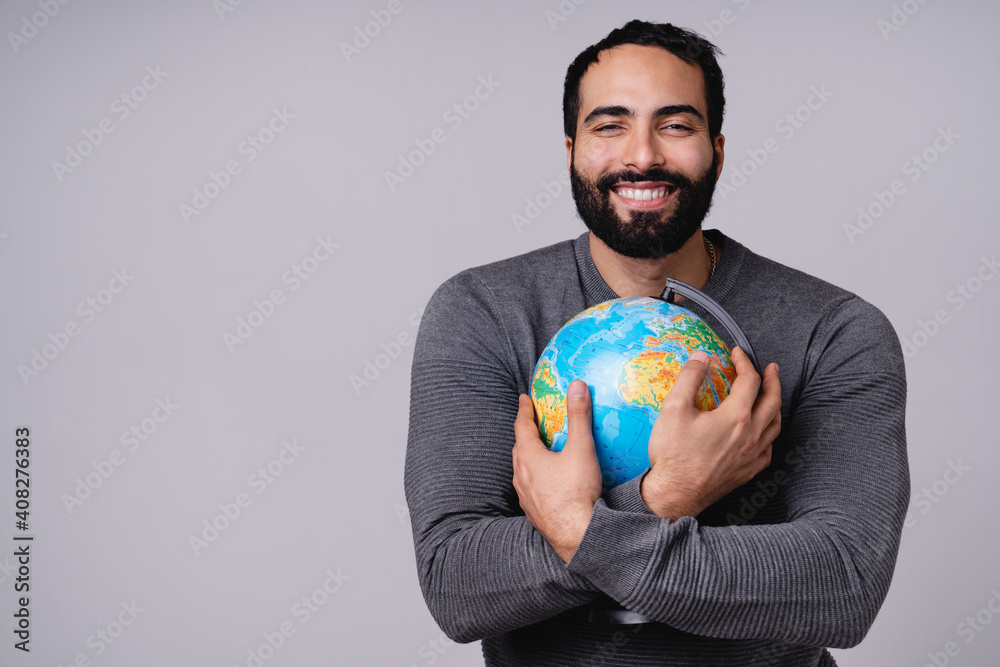 Cheerful adorable young Middle Eastern man holding globe with care and love isolated over grey background. Love the planet concept Cheerful adorable young Middle Eastern man holding globe with care and love isolated over grey background. Love the planet concept