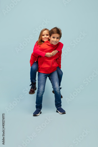 Togetherness. Happy children isolated on blue studio background. Look happy, cheerful. Copyspace for ad. Childhood, education, emotions, facial expression concept. Having fun, playing piggyback
