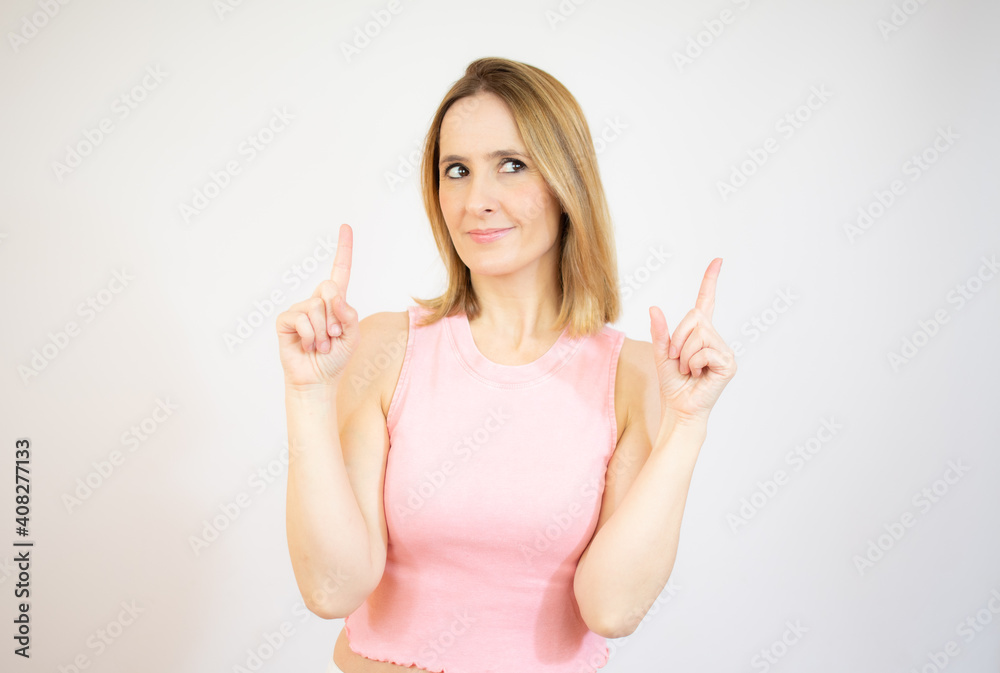 Young woman pointing up with both index fingers while smiling cheerfully away, standing over white background. Young woman pointing up with both index fingers while smiling cheerfully away, standing over white background.