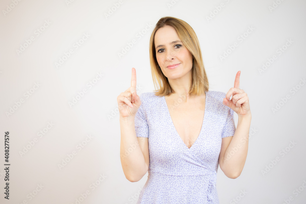 Young woman pointing up with both index fingers while smiling cheerfully at camera, standing over white background. Young woman pointing up with both index fingers while smiling cheerfully at camera, standing over white background.