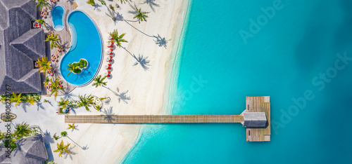 Beautiful aerial view of poolside and resort beach with wooden pier jetty. Luxurious tropical beach landscape, swimming, deck chairs and loungers, umbrellas. Tropical beach, aerial drone top view