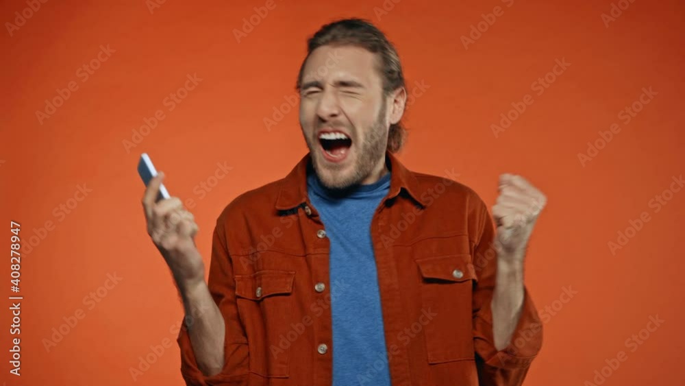 excited man gambling on smartphone and showing win gesture isolated on orange excited man gambling on smartphone and showing win gesture isolated on orange