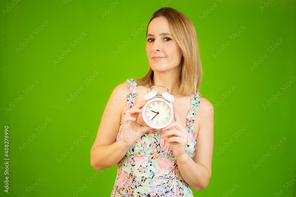 Young woman holding alarm clock standing over isolated green background very happy pointing with hand and finger Young woman holding alarm clock standing over isolated green background very happy pointing with hand and finger