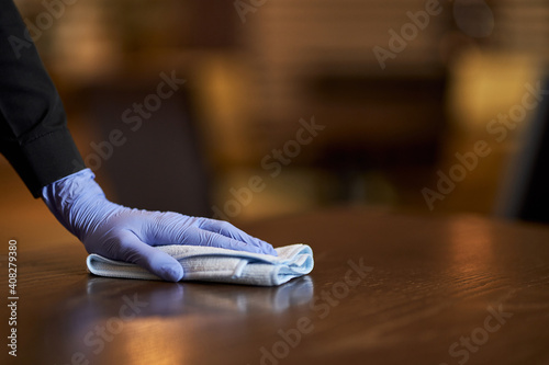 Person with gloves on cleaning and sanitizing a wooden table