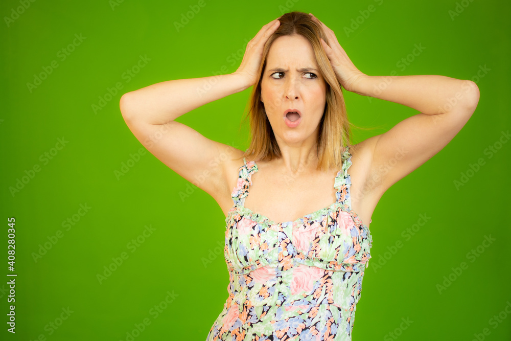young blonde woman feeling horrified and shocked, raising hands to head and panicking at a mistake over green background. young blonde woman feeling horrified and shocked, raising hands to head and panicking at a mistake over green background.