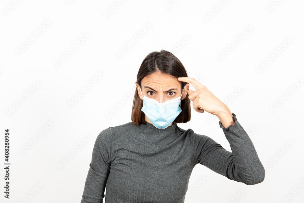 Hispanic woman wearing a medical mask making crazy sign with her finger. Mental health during Coronavirus pandemic concept. Hispanic woman wearing a medical mask making crazy sign with her finger. Mental health during Coronavirus pandemic concept.