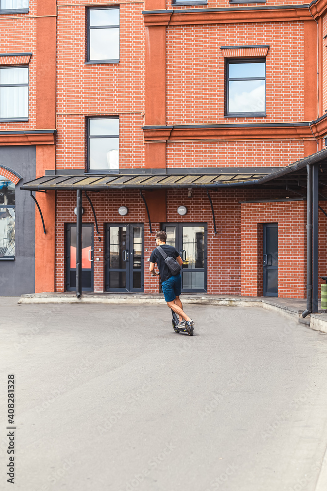 A young man rides around the city on an electric scooter. Vertical photo. Ecological transport