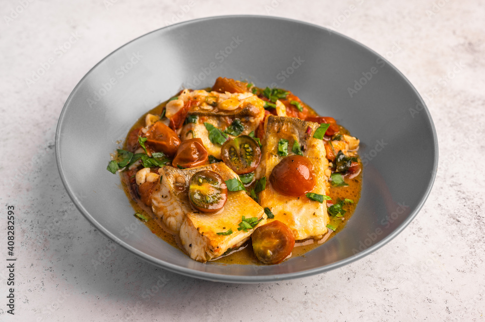 Traditional Sicilian fish with tomatoes, olives, parsley and red pepper in a deep plate on a light background, close up Traditional Sicilian fish with tomatoes, olives, parsley and red pepper in a deep plate on a light background, close up