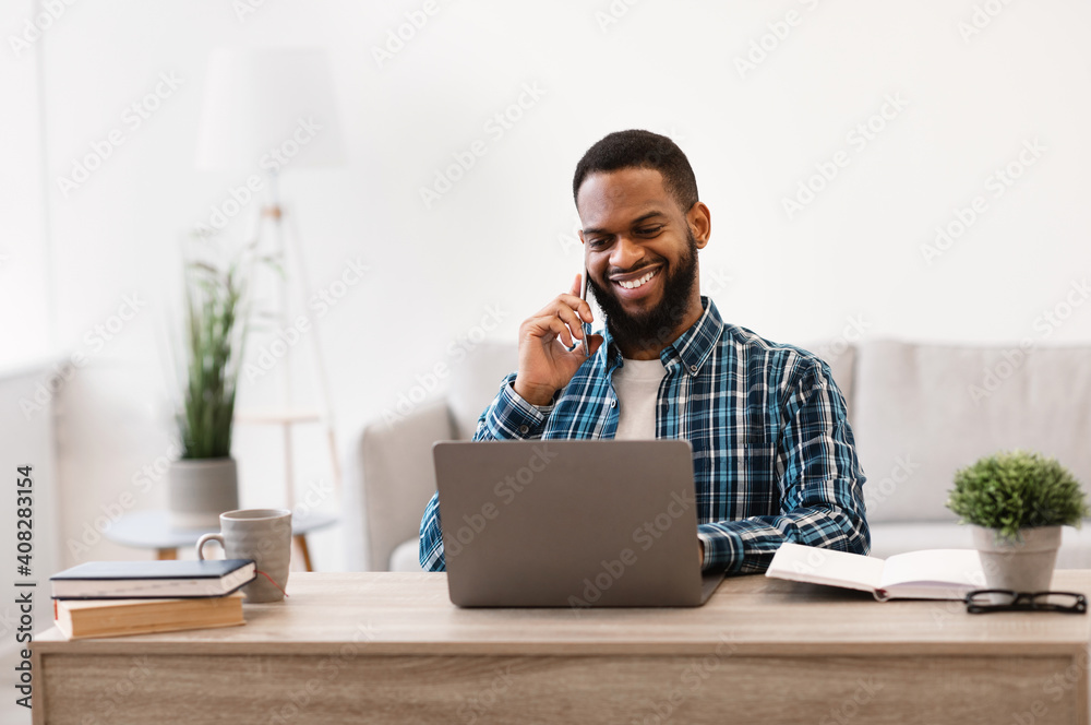 African Businessman Talking On Cellphone Sitting At Laptop In Office - obrazy, fototapety, plakaty 