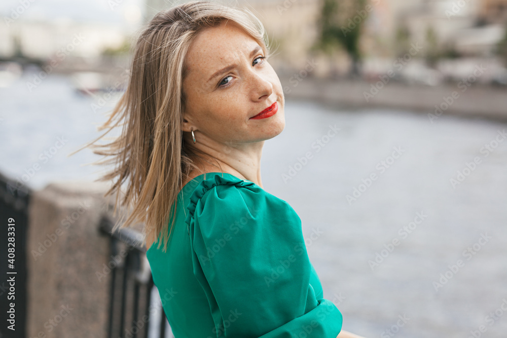 portrait of a beautiful smiling young woman with red lipstick and in a green dress on the background of the river embankment in the city portrait of a beautiful smiling young woman with red lipstick and in a green dress on the background of the river embankment in the city