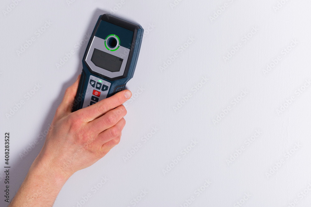 Man hand is scanning wall by cable detector to find a cable before drilling in.