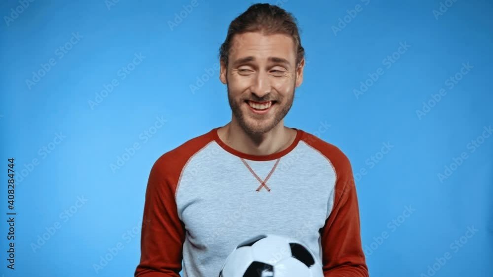 cheerful man with soccer ball showing come with me gesture isolated on blue cheerful man with soccer ball showing come with me gesture isolated on blue