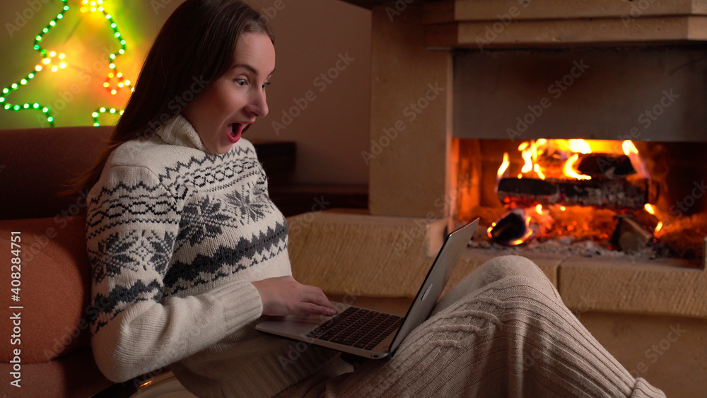 Young woman celebrates success or a happy pose with a laptop in front of a fireplace Young woman celebrates success or a happy pose with a laptop in front of a fireplace