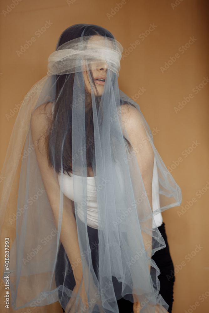 Photo portrait of brunette woman hiding eyes behind grey tulle on brown color background Photo portrait of brunette woman hiding eyes behind grey tulle on brown color background