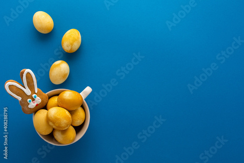 Easter yellow painted eggs and biscuits bunny in a mug on bright blue background, easter festive concept