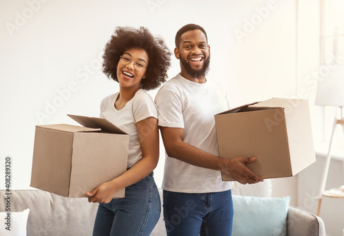 Joyful Black Couple Moving House Posing Holding Packed Boxes Indoors