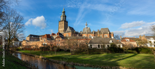 Panorama cityscape of medieval Hanseatic city Zutphen in The Netherlands against a blue sky with clouds lit up by afternoon sun with lush winter garden in the foreground