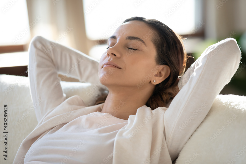 Close up calm woman with closed eyes relaxing on couch, leaning back, sitting with hands behind head, attractive young female enjoying lazy weekend, daydreaming, taking nap, stress relief