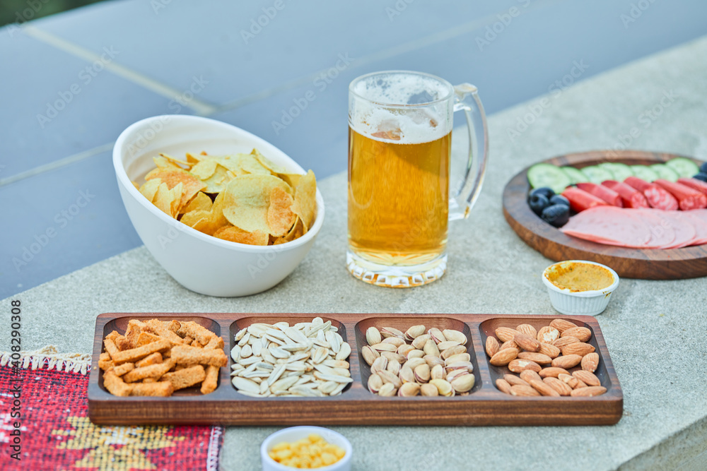 Assorted snacks, chips, a plate of sausages and a glass of beer on stone table